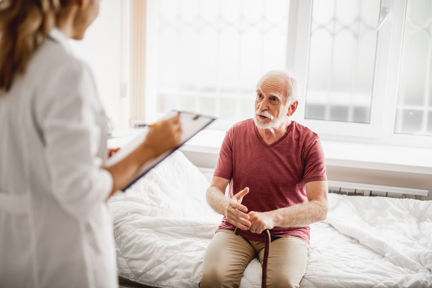 Old man sitting on hospital bed and having conversation with doctor